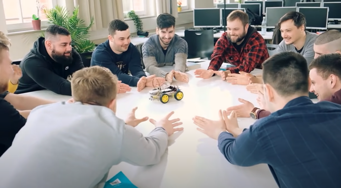 Schüler der Techniker Schule sitzen lachend am Tisch und betrachten ein kleines Elektroauto